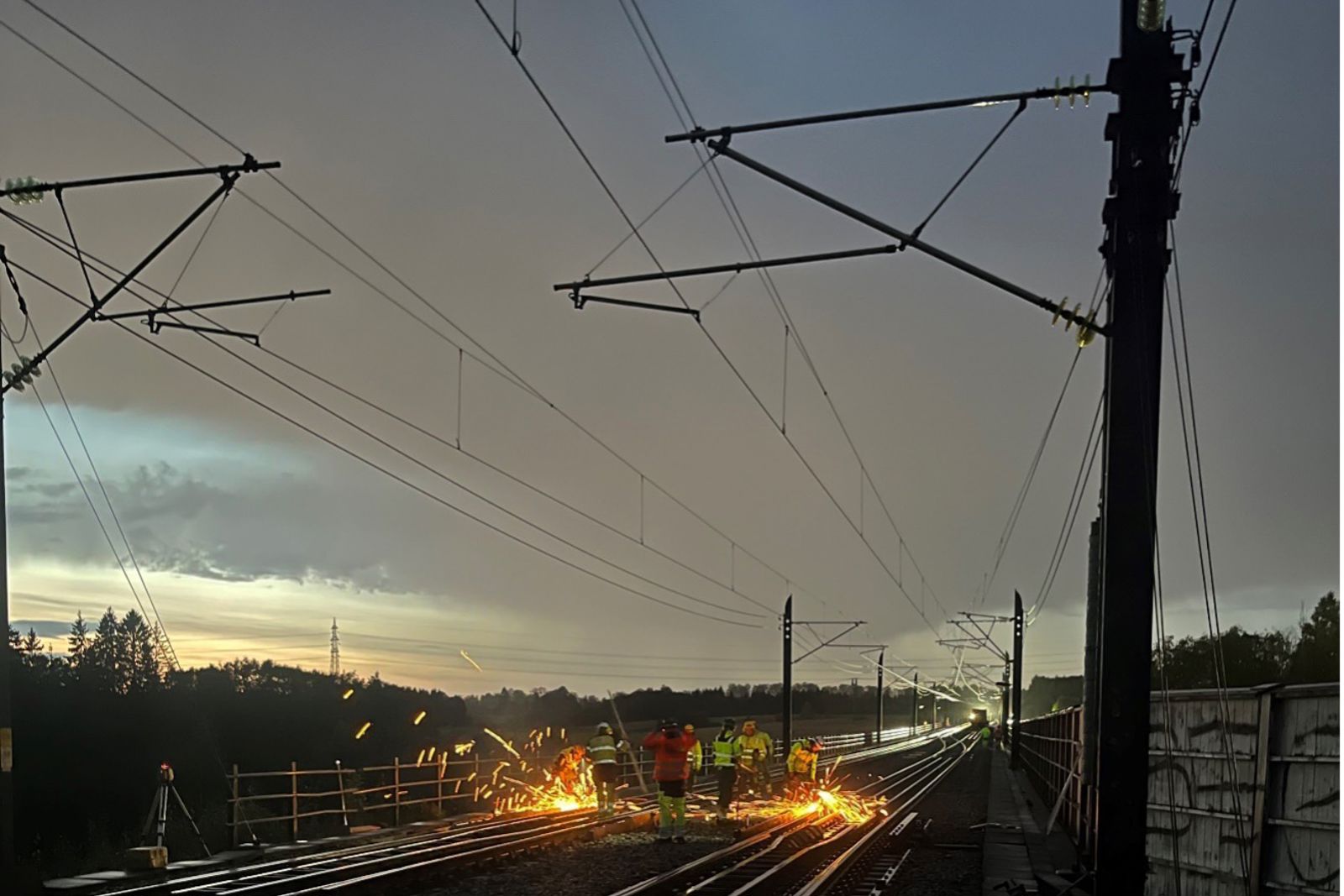 Arbeidere står i sporet i mørket, man ser store gnister.