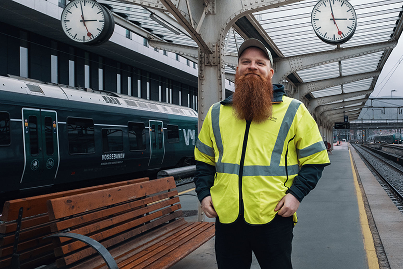 En mann i gul vest står på perrongen med et tog i bakgrunn.