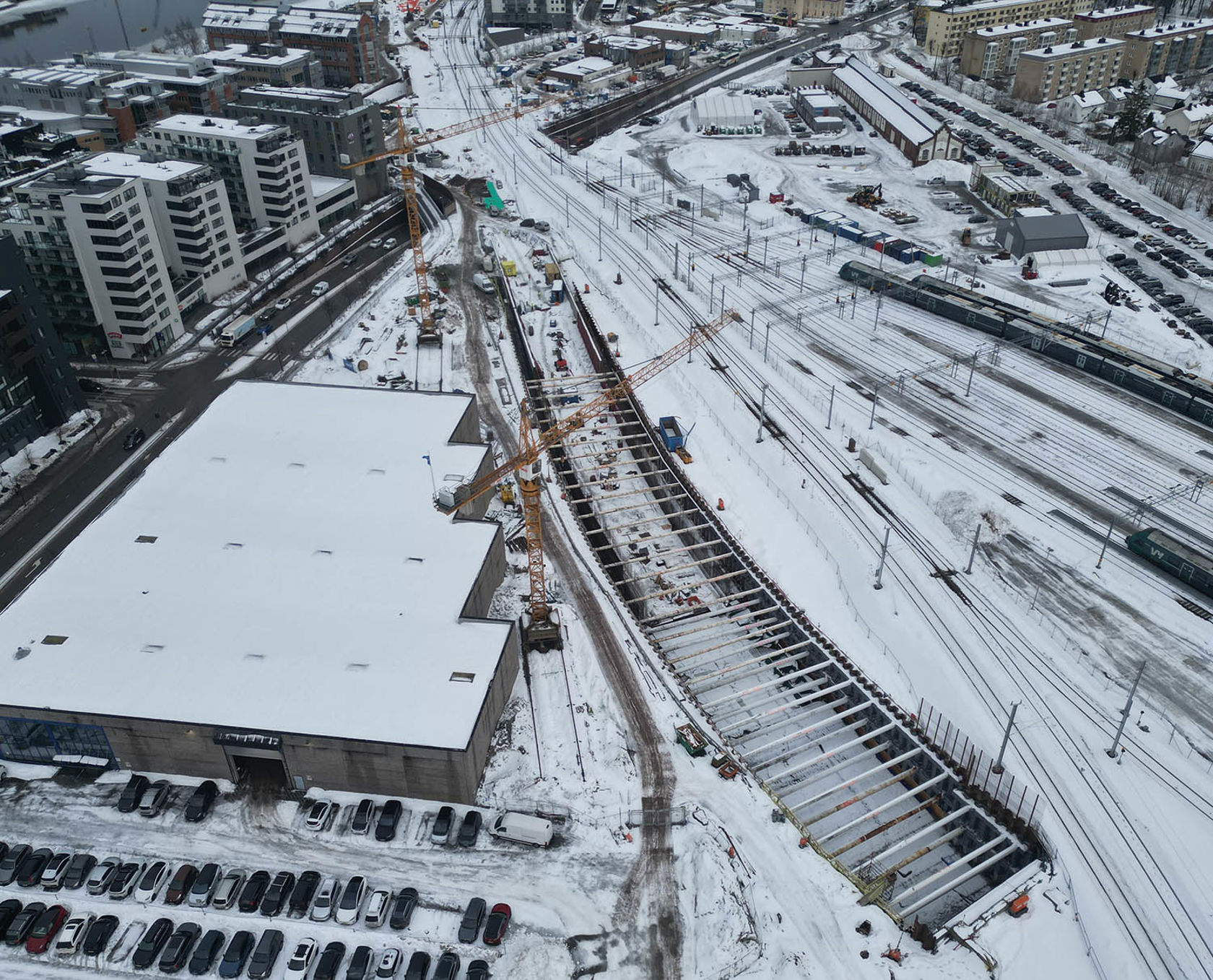 Byggeplass nær togspor med kraner og snø.