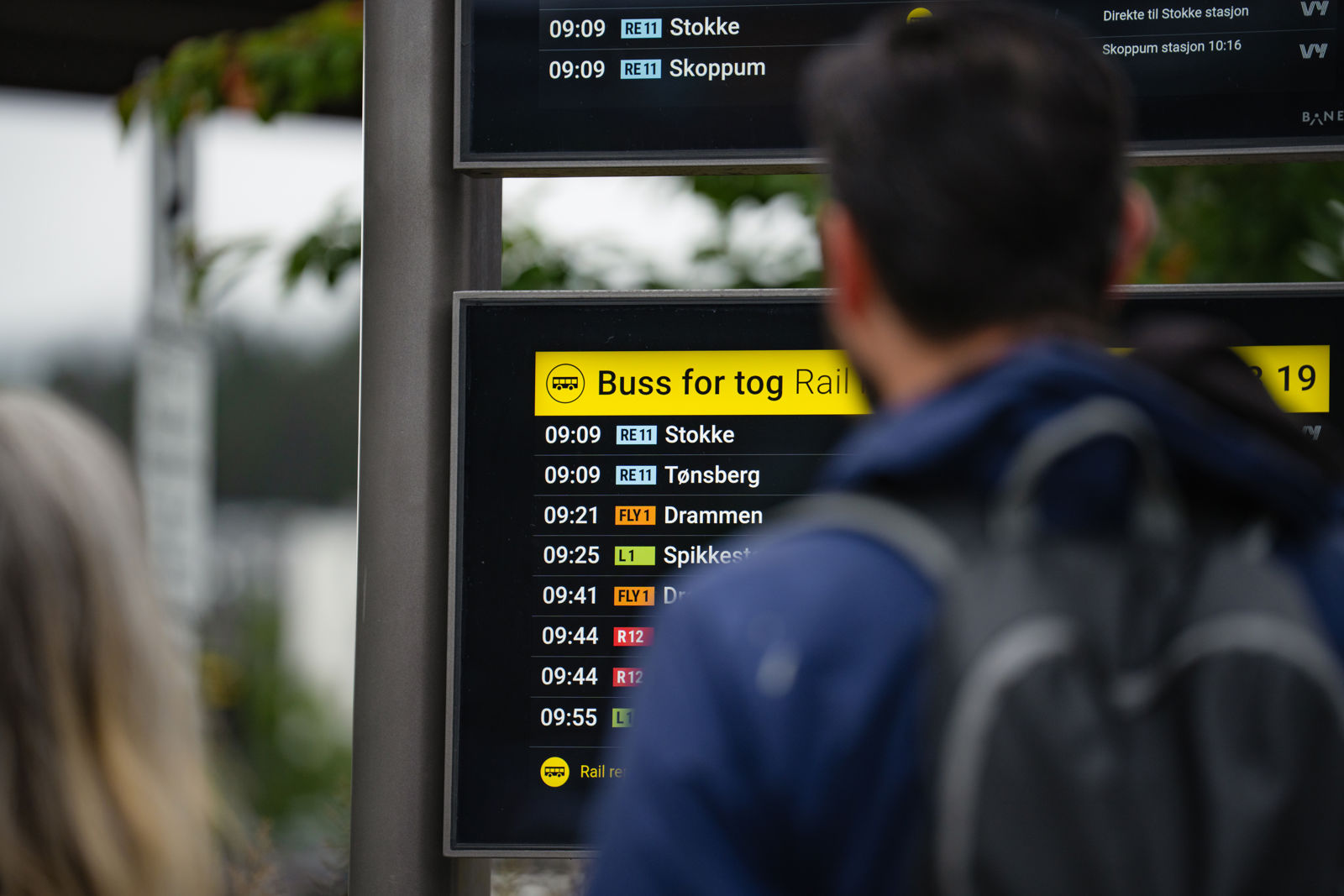 Reisende ser på monitor med avgangstider for buss for tog.