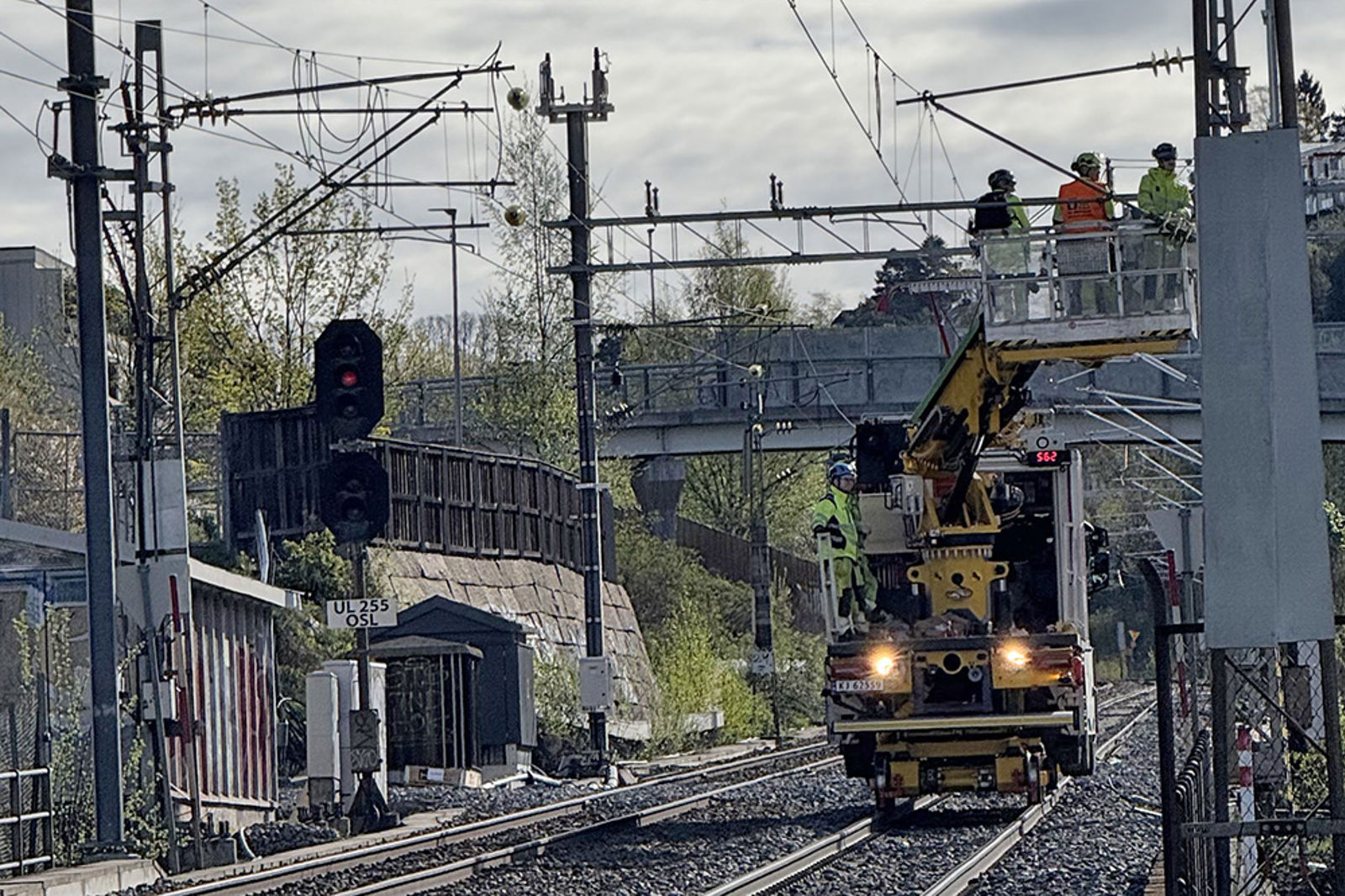 Arbeidsmaskin på sporet, tre personer i en lift jobber med kontaktledningen.