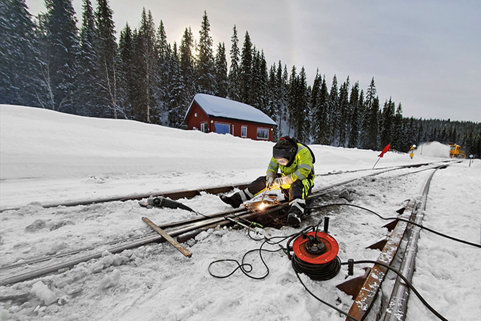 En person sitter på baken midt i et spor og sveiser skinnegangen.