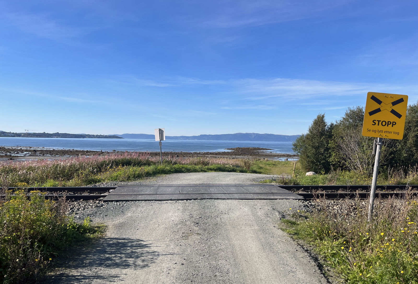 Enkel planovergang i kystlandskap med havet i bakgrunn.