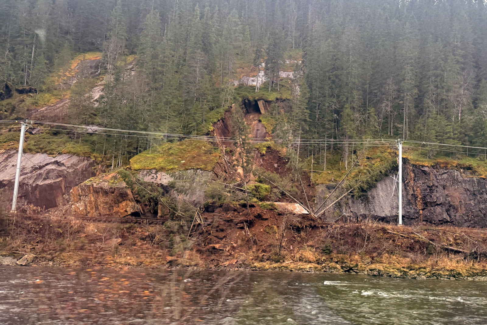 Bildet er tatt fra motsatt side av elva og viser at jord- og steinmasser har rast ut i sporet.