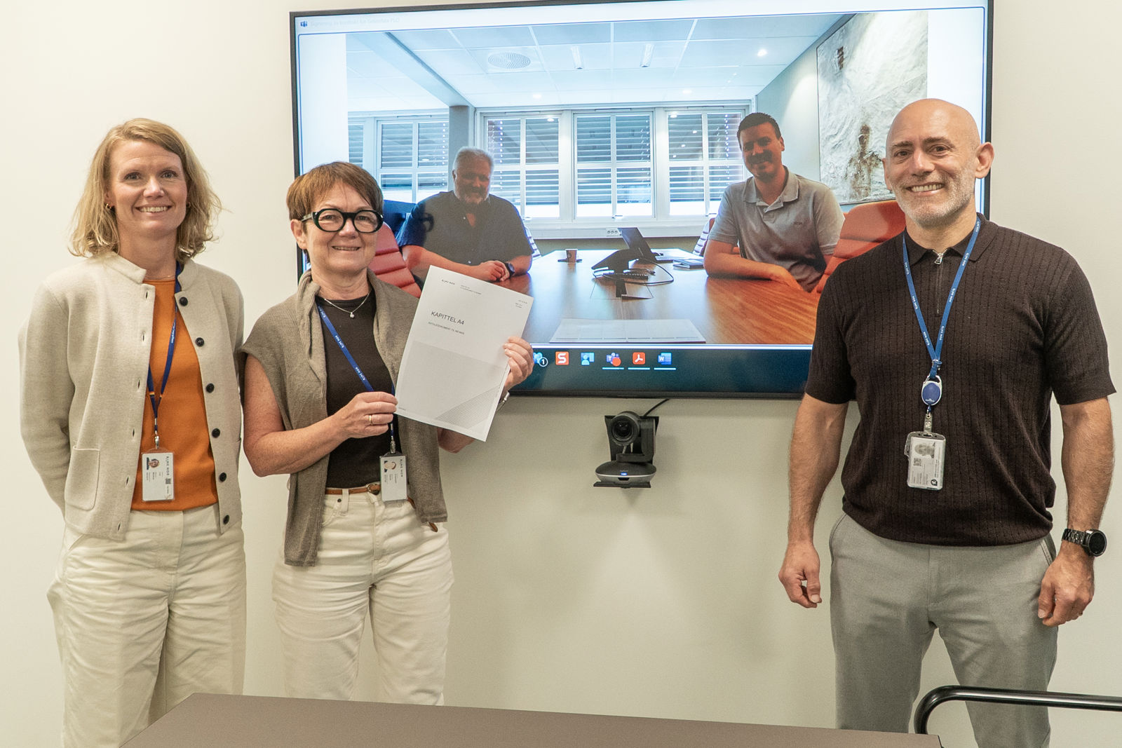 To kvinner og en mann står foran en skjerm der to menn er avbildet